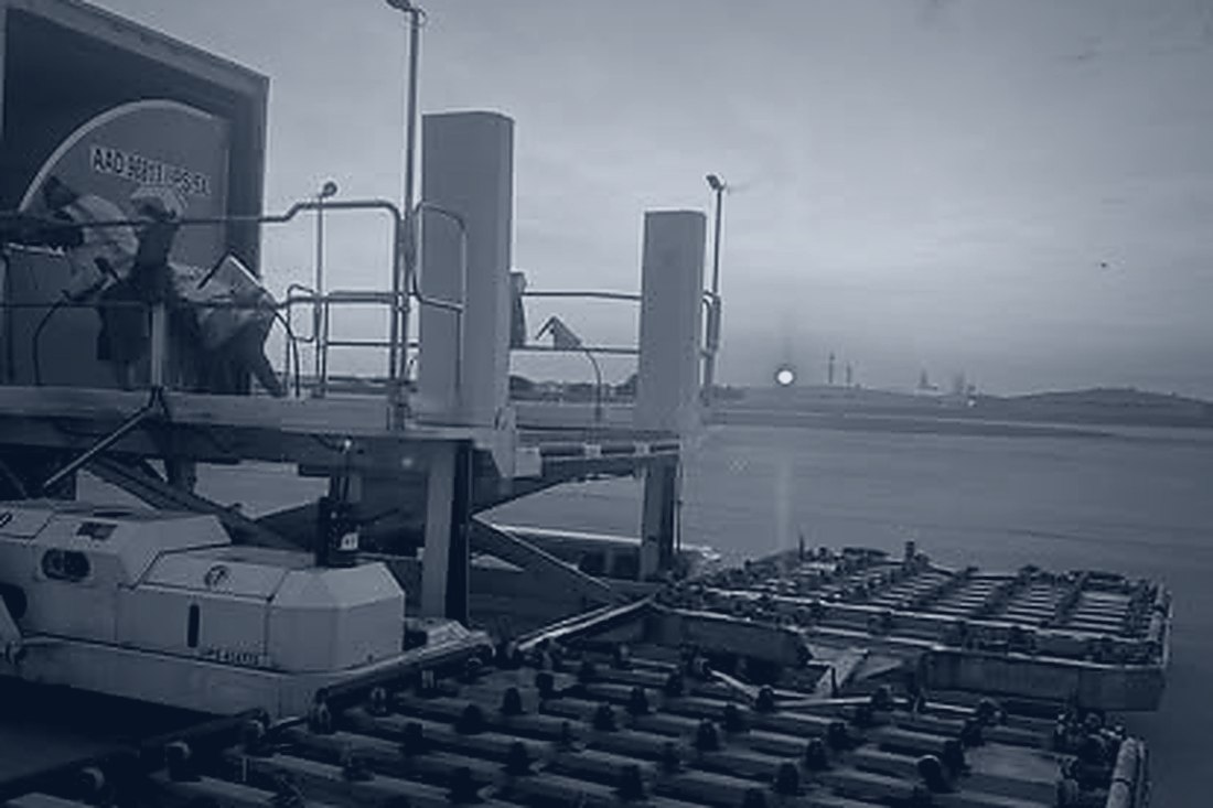 Roller-bed deck in the foreground with a scissor loader working a ULD on the ramp at sunrise